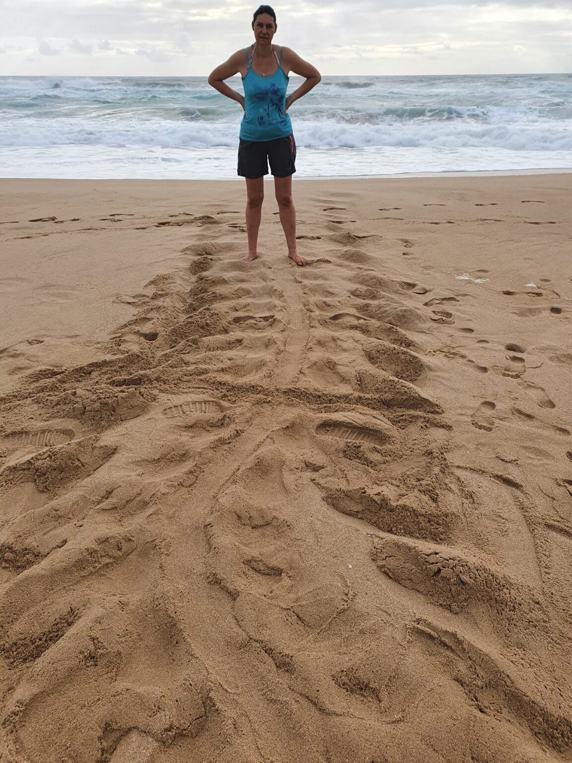 Person standing on beach with arms wide, turtle tracks on foreground.